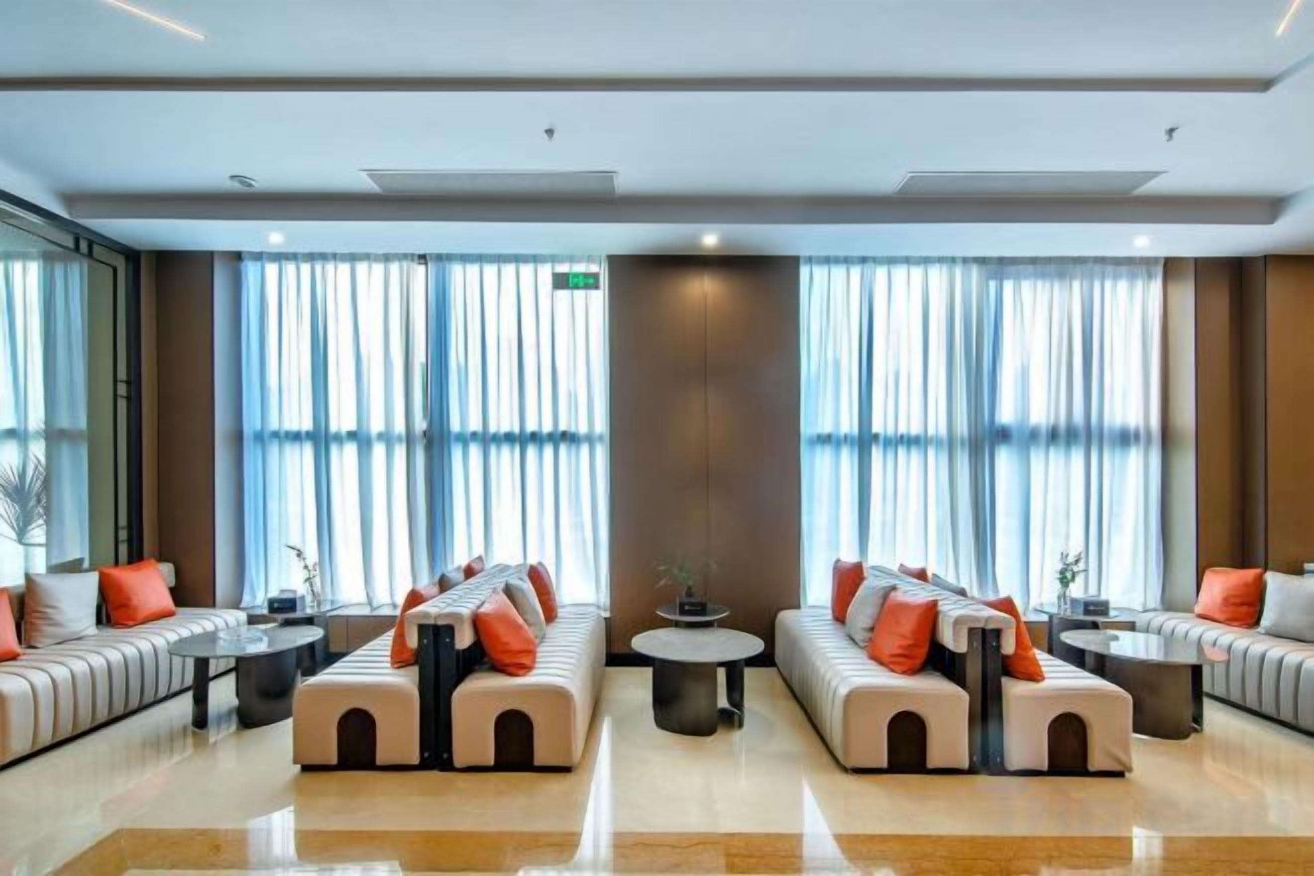A hotel lobby with two seating areas, a coffee table, and large windows with curtains.