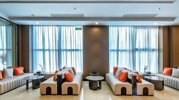 A hotel lobby with two seating areas, a coffee table, and large windows with curtains.