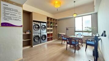 A laundry room with stacked washers and dryers, a dining area with a table and chairs, and a large window providing natural light.