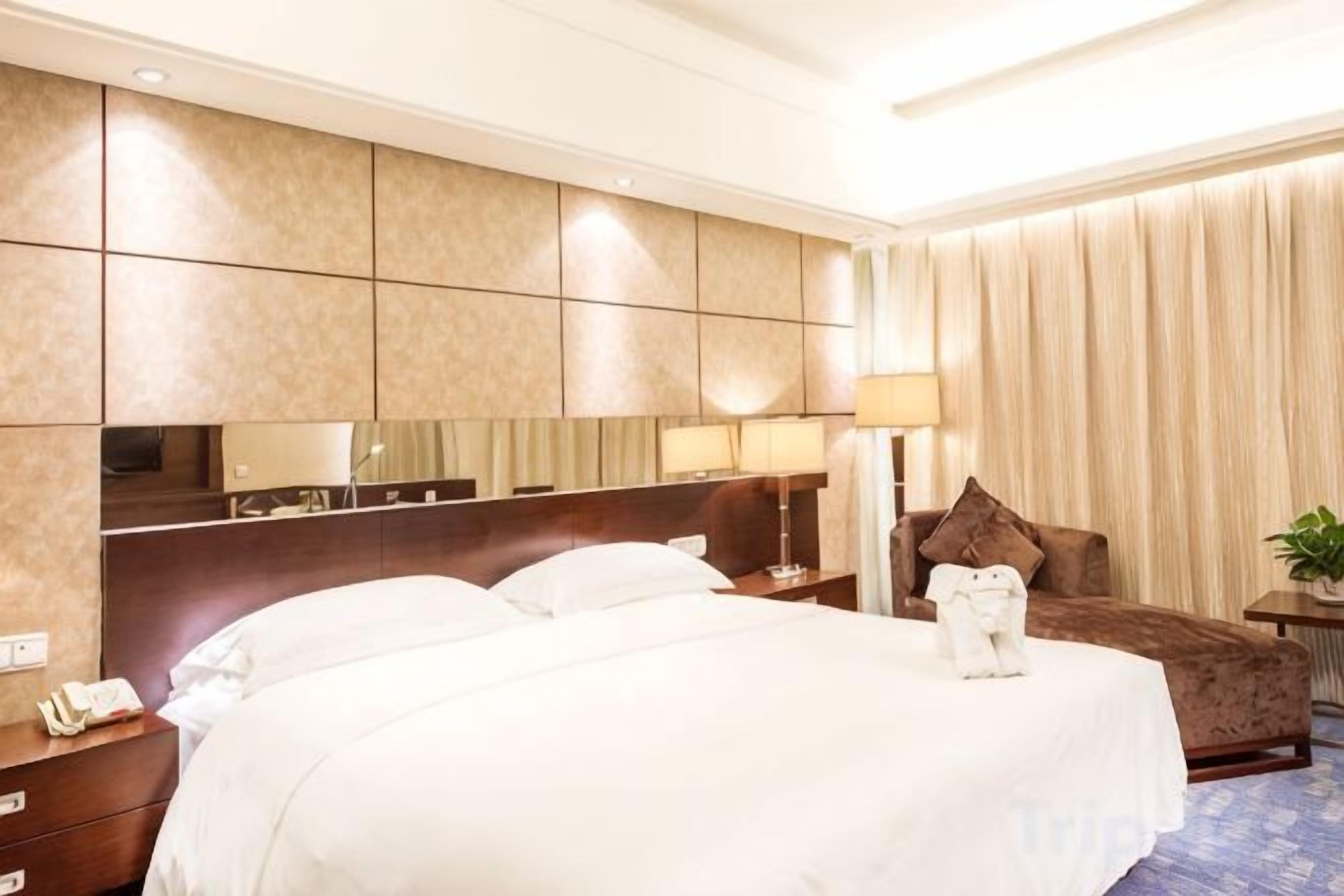Ein Hotelzimmer mit einem großen Bett, einem Nachttisch mit Telefon, einer Lampe, einem Sessel und einem Spiegel.
