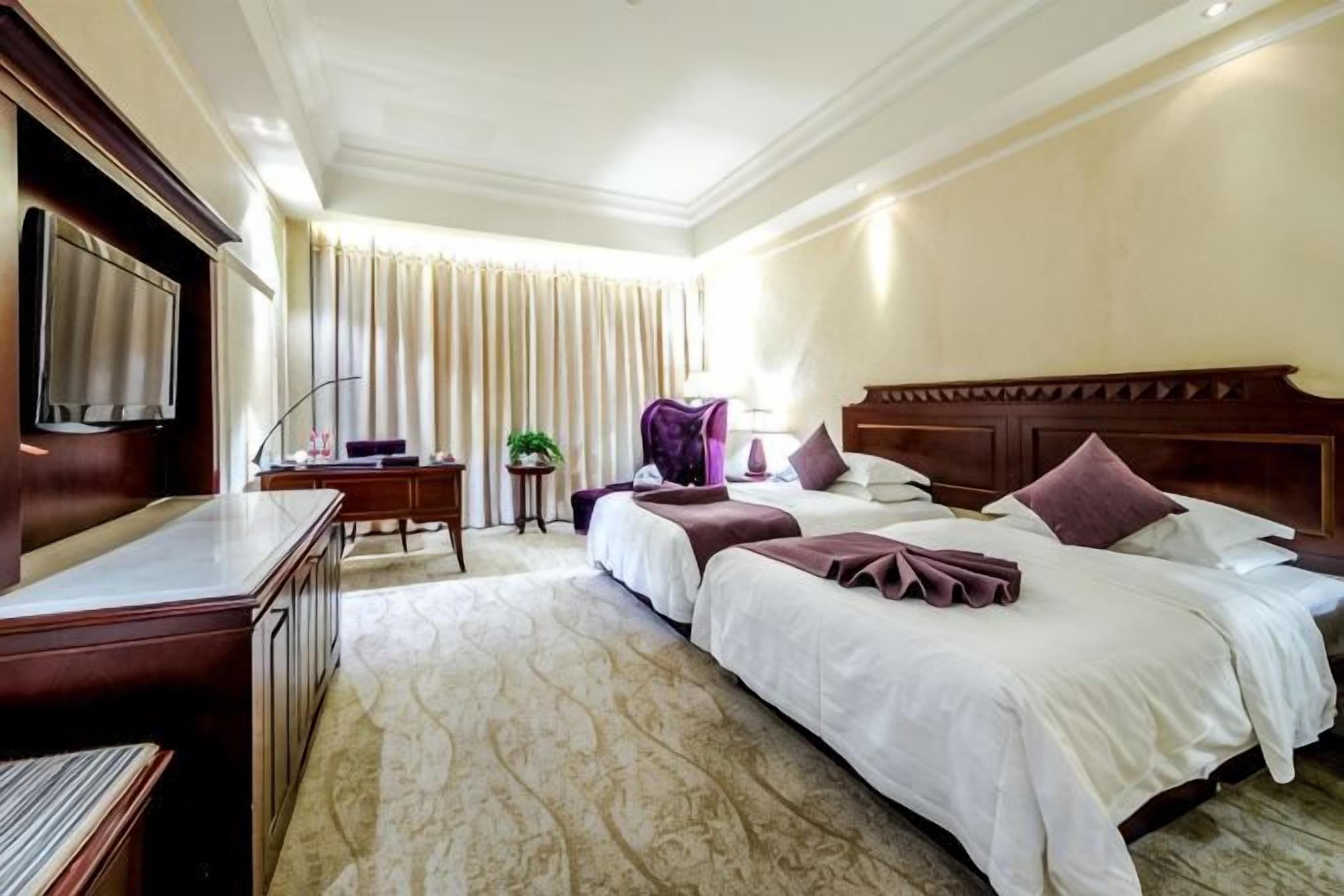 A hotel room with a bed, a desk, a chair, a television, and a window with curtains.