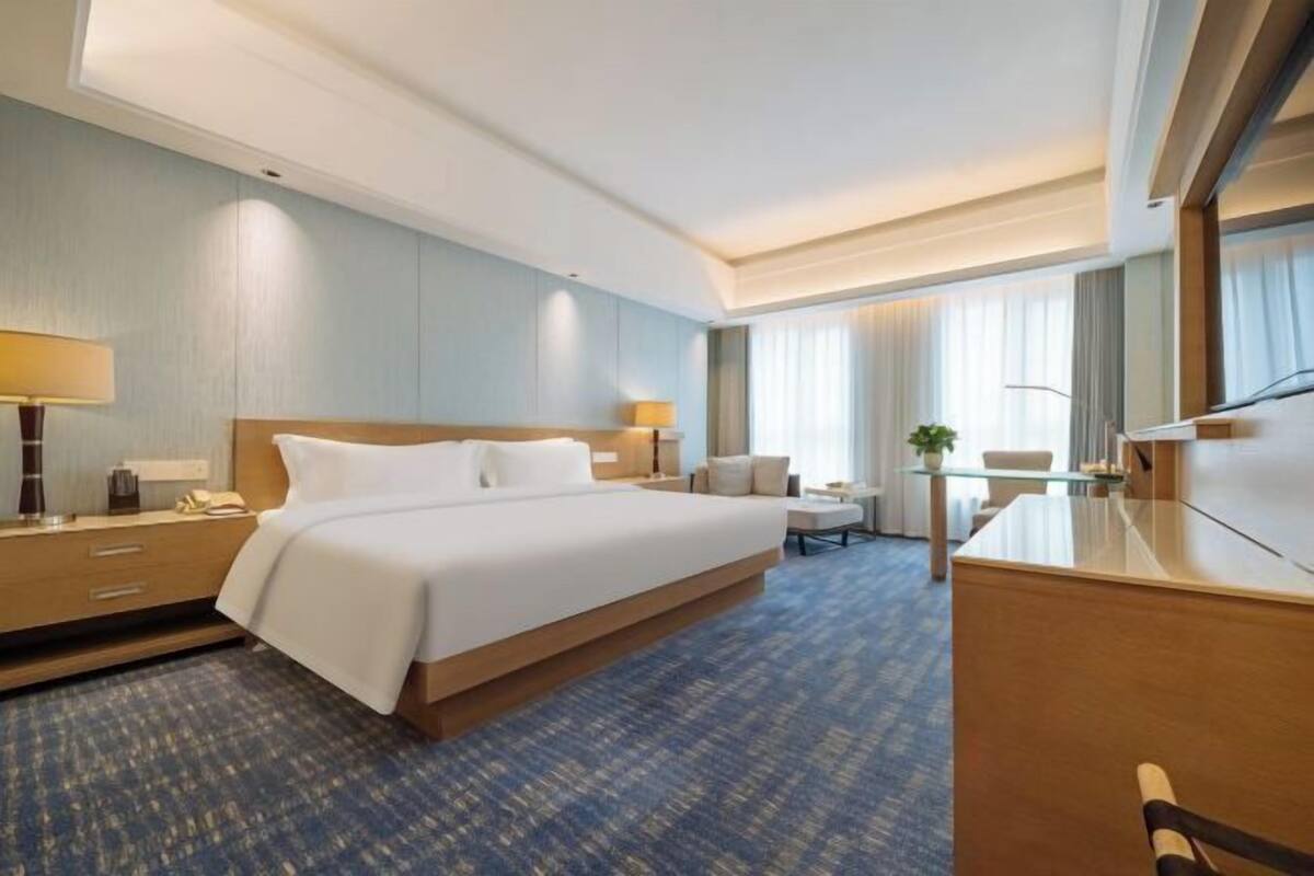 Hotellihuone, jossa on suuri sänky, työpöytä, tuoli, lamppu ja peili.