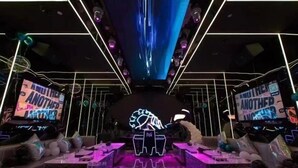 Un escenario con luces de neón y una pantalla grande que muestra 'ANOTHER ANOTHER ANOTHER'.