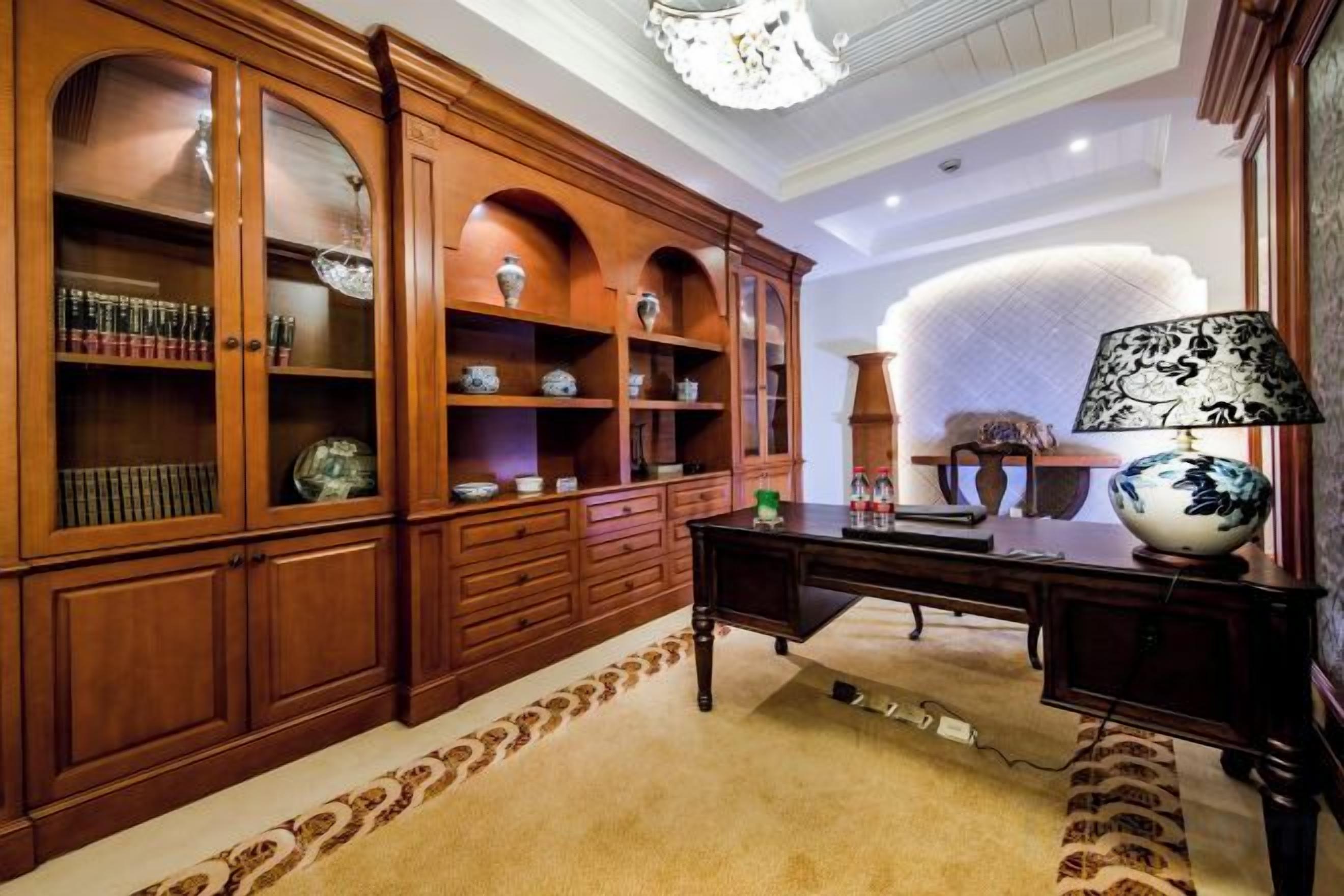 A room with a large wooden cabinet, a desk with a lamp, and a patterned rug.