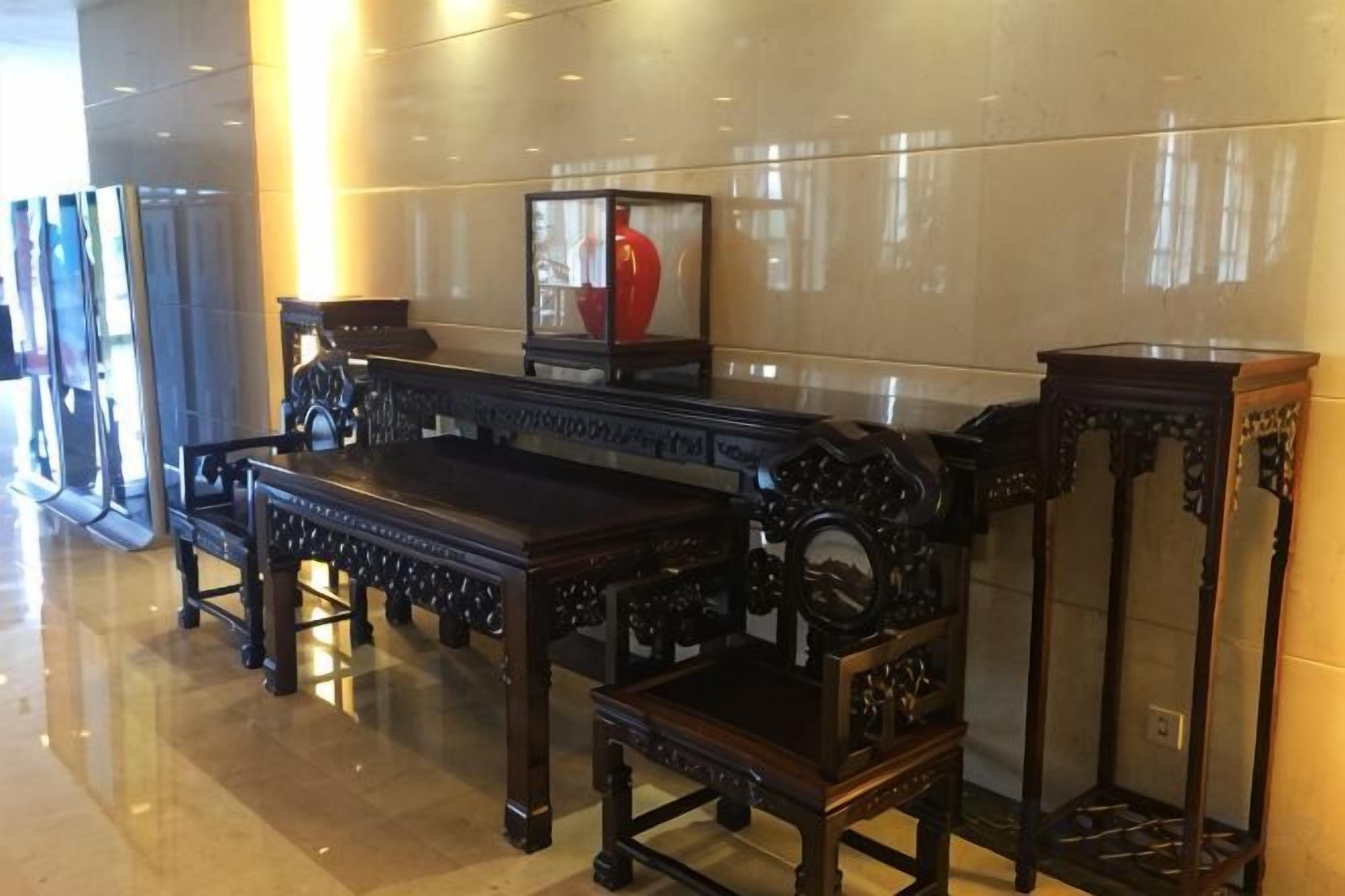 A polished lobby with a long, ornate wooden bench and a tall, narrow table with intricate carvings.