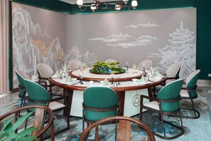 A round table with six chairs, a floral centerpiece, and a wall mural with traditional artwork. - Haizhou Hotel (Haining)