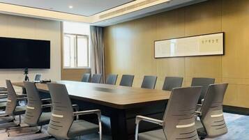 A conference room with a long table, multiple chairs, a flat-screen TV, and a projector.
