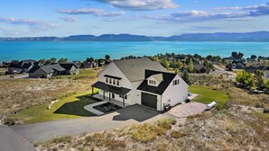 A large white house with a garage, surrounded by a well-maintained lawn and a view of a lake and mountains. - Raspberry Retreat ~ Private Hot Tub ~ Indoor Pickleball (Garden City)