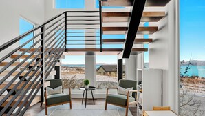 A modern interior with a staircase, two armchairs, a small table, and a view of the outdoors. - Raspberry Retreat ~ Private Hot Tub ~ Indoor Pickleball (Garden City)