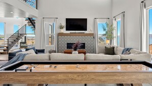 A spacious living room with a large flat-screen TV, a sectional sofa, a wooden coffee table, and a staircase leading to an upper level. - Raspberry Retreat ~ Private Hot Tub ~ Indoor Pickleball (Garden City)