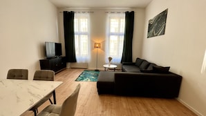 Una sala de estar con sofá, televisión, mesa de comedor y sillas, y una lámpara.