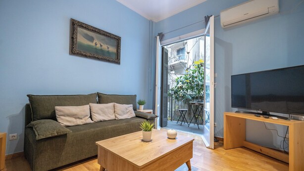 A living room with a sofa, a coffee table, a TV on a stand, and a sliding glass door leading to an outdoor area. - Central Athens Apt Patio View by MPS (Athina)