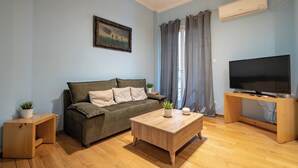 A living room with a sofa, a coffee table, a TV on a stand, and a painting on the wall. - Central Athens Apt Patio View by MPS (Athina)