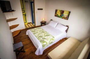 A bedroom with a bed, a chair, a nightstand, a painting, and a television on a shelf. - FINCA HOTEL BARILOCHE (Santa Rosa de Cabal)