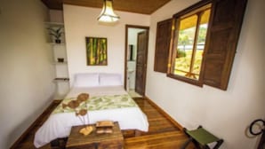 A bedroom with a wooden floor, a bed with a green and white bedspread, a wooden nightstand, a small table with a vase, and a window with wooden shutters. - FINCA HOTEL BARILOCHE (Santa Rosa de Cabal)