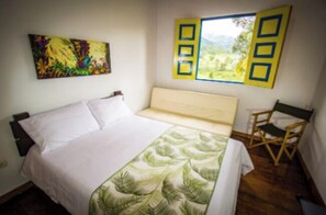 A bedroom with a bed, a window with a view, a painting, and a director's chair. - FINCA HOTEL BARILOCHE (Santa Rosa de Cabal)