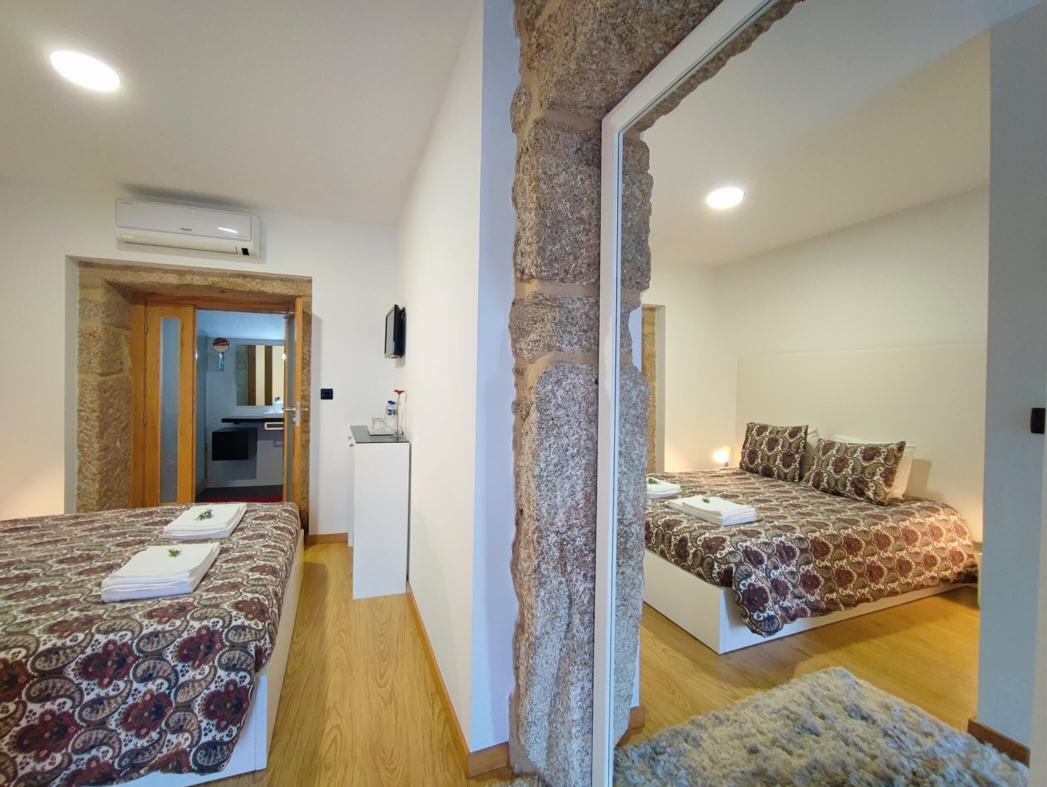 Ett modernt hotellrum med två sängar, ett litet pentry och en vägg som är accentuerad med sten.
