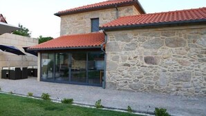 A stone building with a tiled roof, a glass door entrance, and a paved patio area. - Casa do Parada | Private Pool | Rural Refuge (Messegães Monção)