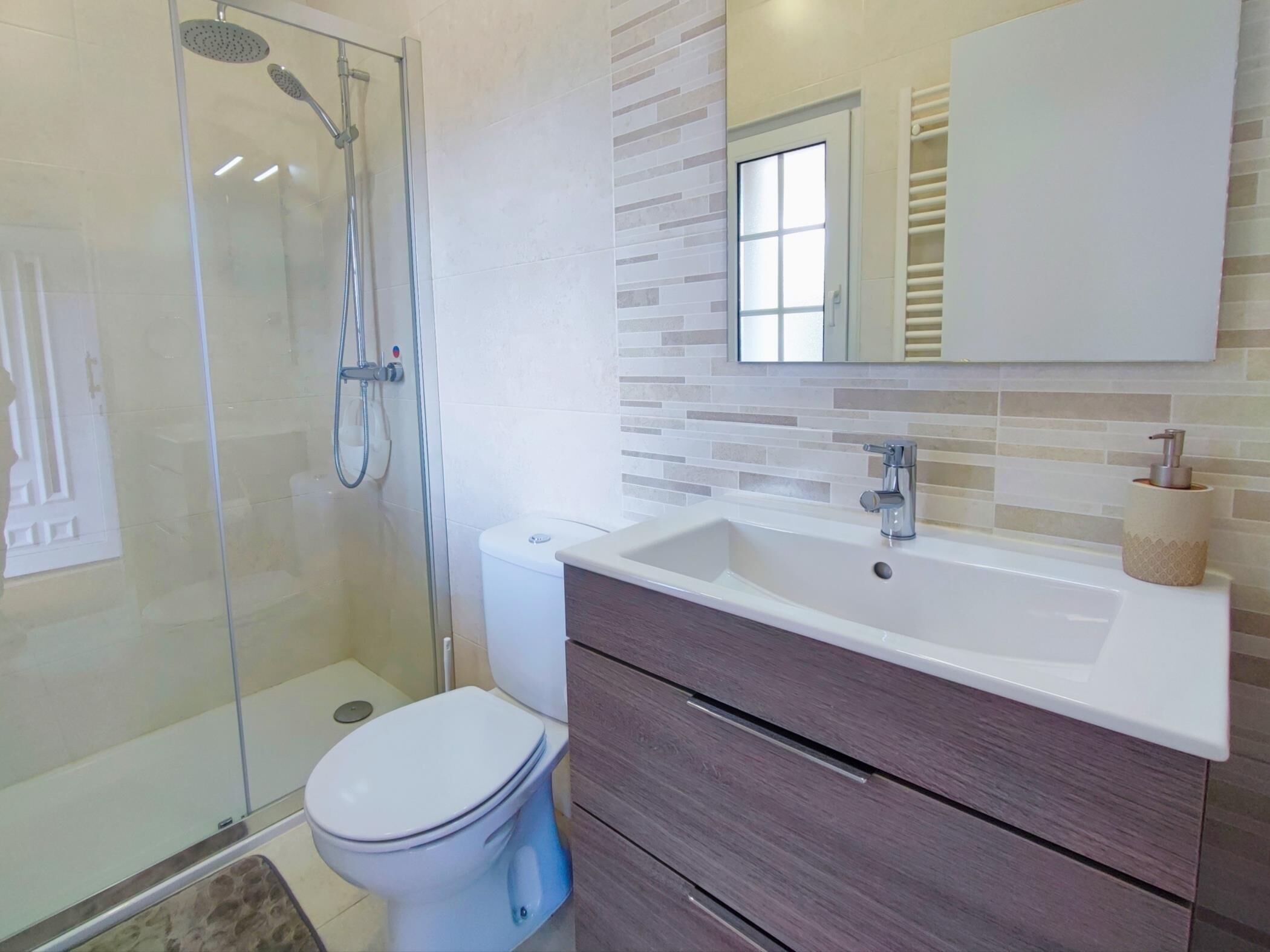 A bathroom with a glass-enclosed shower, a white toilet, a vanity with a mirror, and a sink.