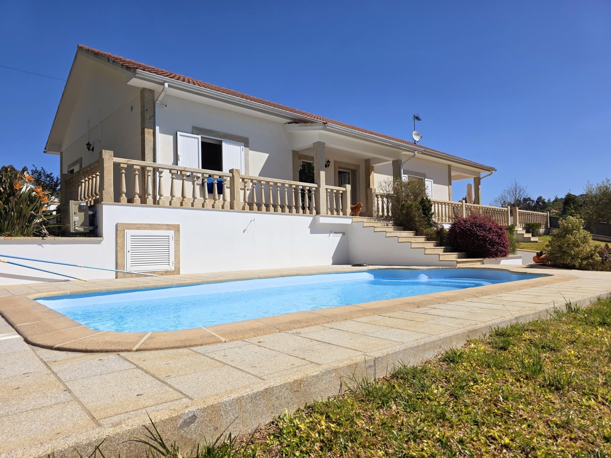 Una casa de dos pisos con piscina, un porche cubierto y un perro en el balcón.