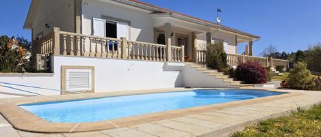 Una casa de dos pisos con piscina, un porche cubierto y un perro en el balcón.
