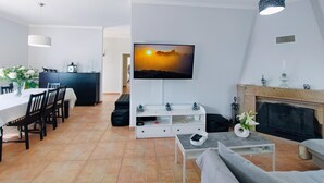 A modern living room with a flat-screen TV, a fireplace, and a dining area with chairs and a table.