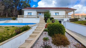 A two-story house with a red-tiled roof, a front porch, and a swimming pool.