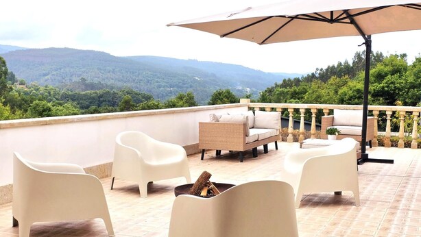 A terrace with white chairs, a wicker sofa, and a large umbrella.
