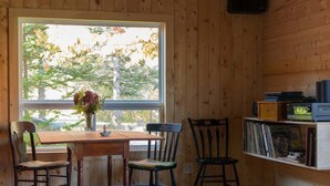Un intérieur en bois avec une table et des chaises, une fenêtre donnant sur des arbres et une étagère remplie de disques.