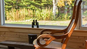 Un fauteuil à bascule placé près d’une fenêtre donnant sur les arbres, ainsi qu’un banc muni de jumelles.
