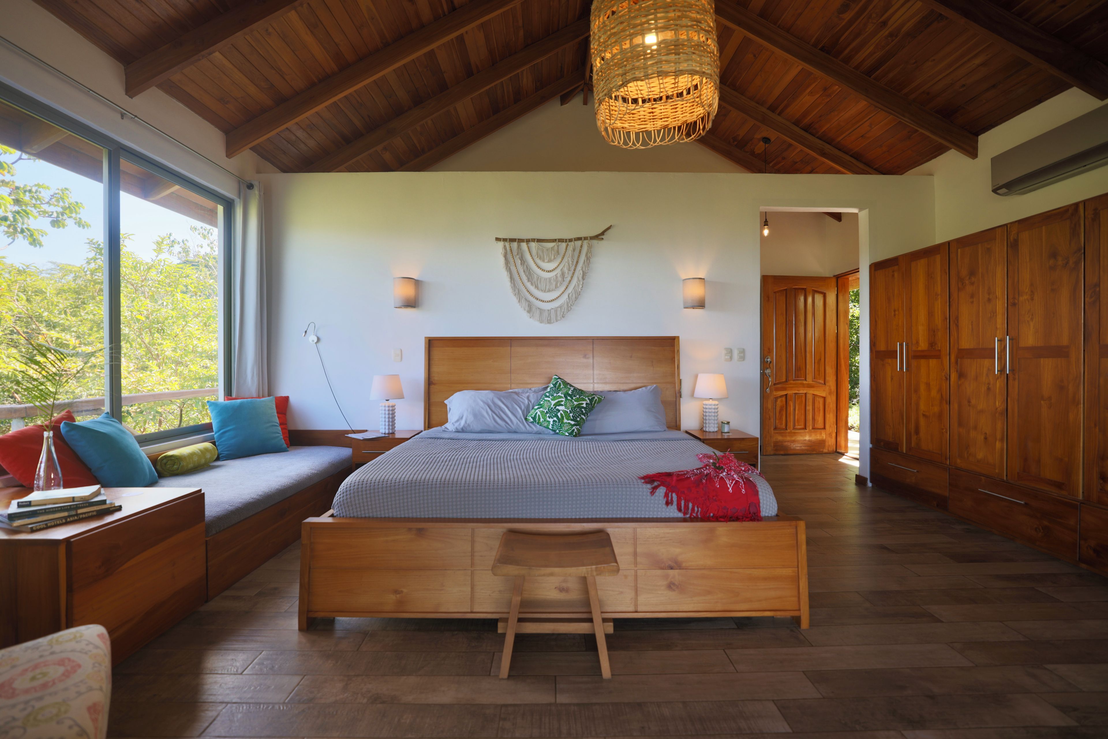 A spacious bedroom with a large bed, wooden furniture, and a view through a window.