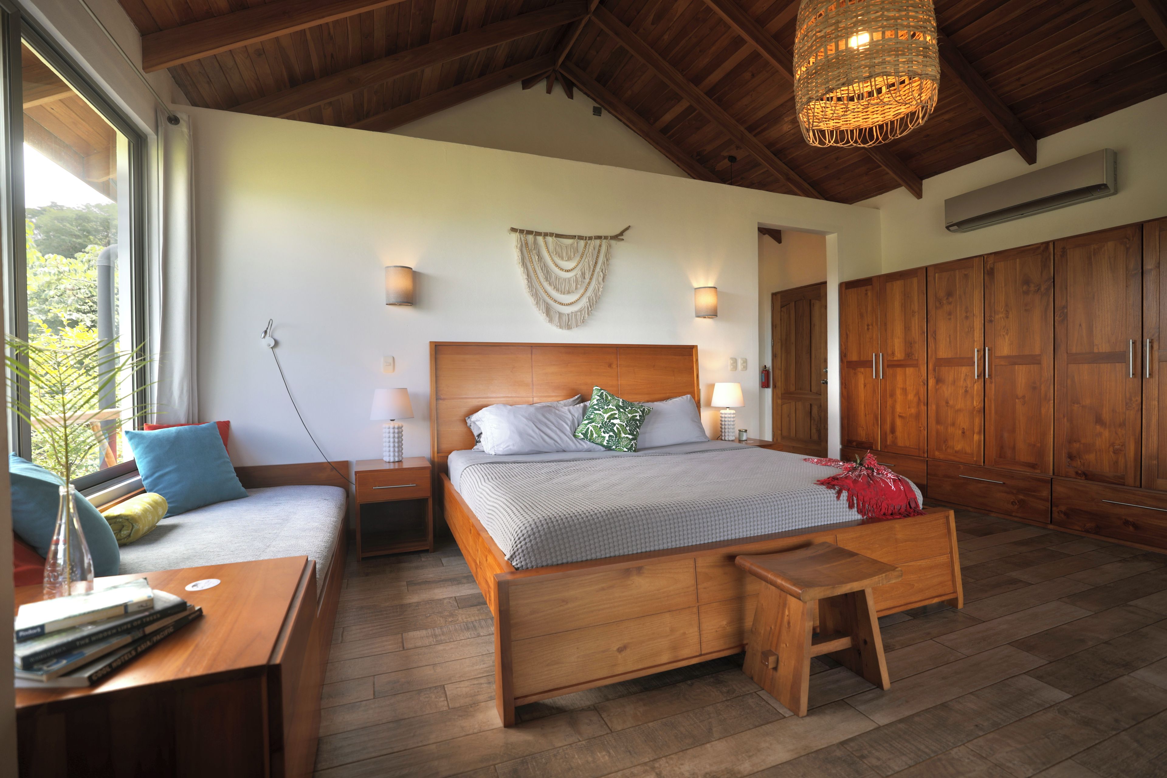 A bedroom with a large bed, wooden furniture, a bedside table, a nightstand, a hanging light fixture, a wall-mounted lamp, and a wardrobe.