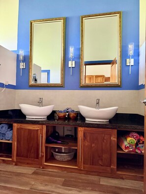 Ein Badezimmer mit zwei weißen Waschtüben, Holzschränken, einem Spiegel und Wandleuchten.