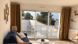 Ein modernes Wohnzimmer mit einem blauen Sofa, einem Holzesstisch und Blick auf einen Balkon mit Geländer.