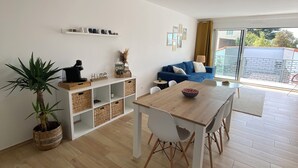 Ein modernes Wohnzimmer mit einem Holzesstisch, weißen Stühlen, einem blauen Sofa und einem großen Fenster mit Blick auf Grünflächen.