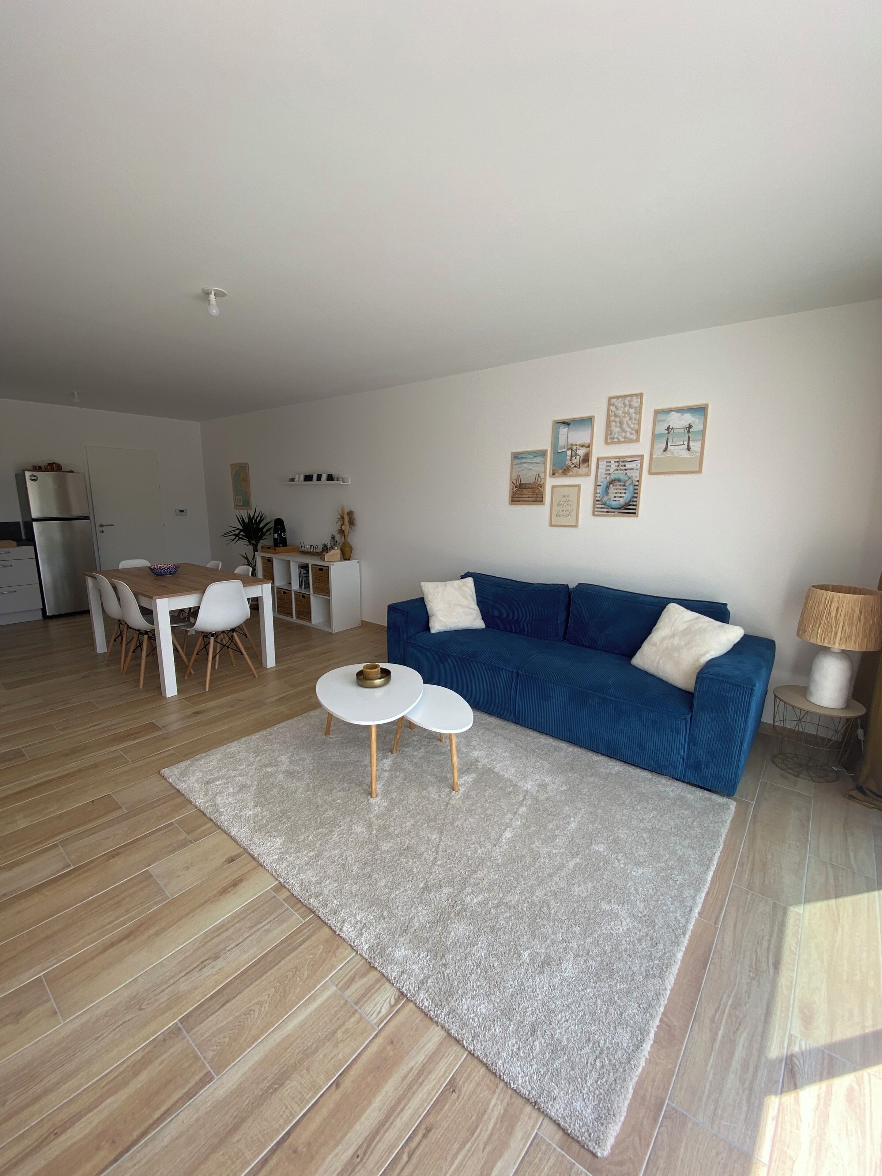 Un salon moderne avec un canapé bleu, une petite table blanche et une cuisine en arrière-plan.