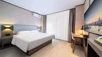 A hotel room with a bed, bedside table, desk, chair, and a large window with curtains.