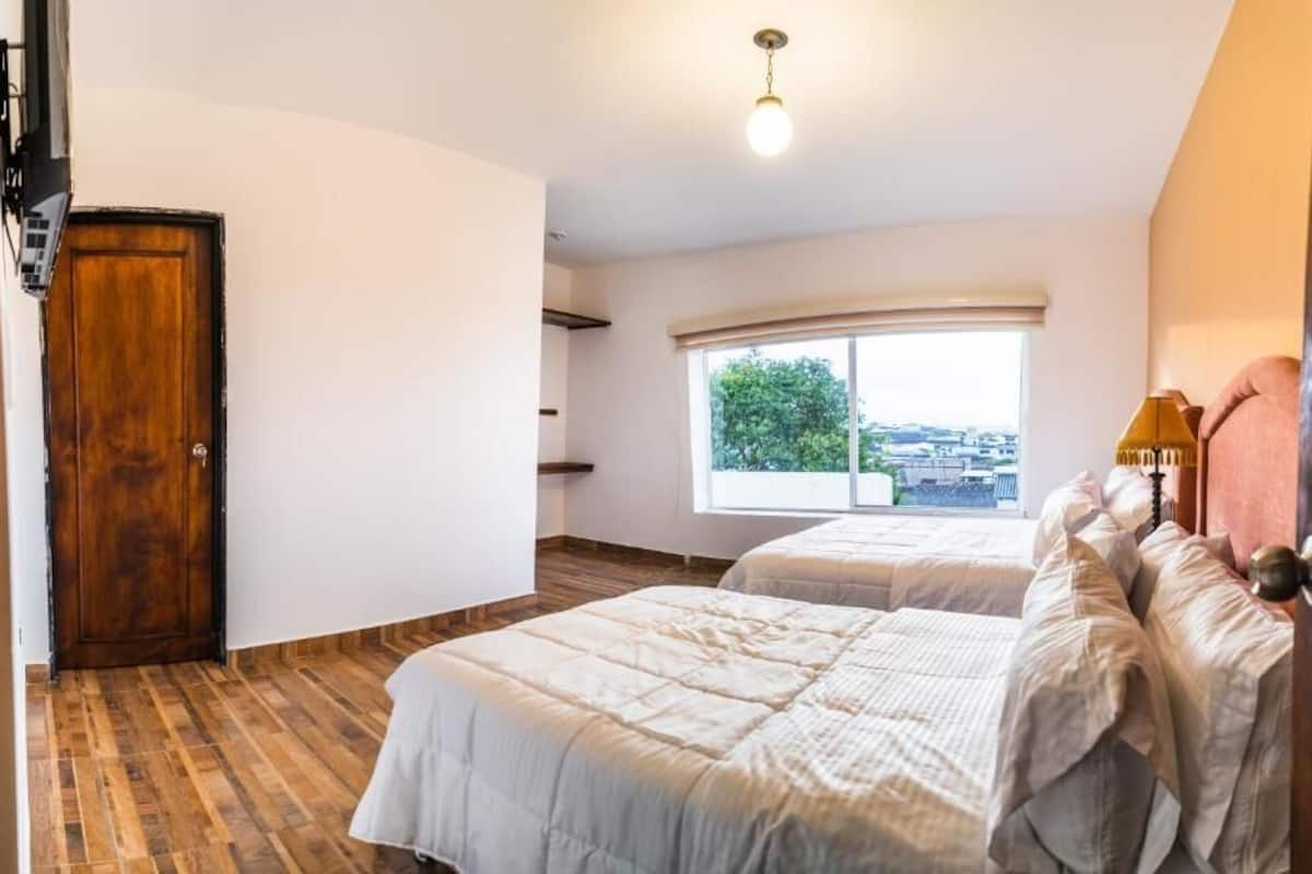 Une chambre avec deux lits, une porte en bois, une fenêtre donnant sur un paysage agréable et un luminaire au plafond.