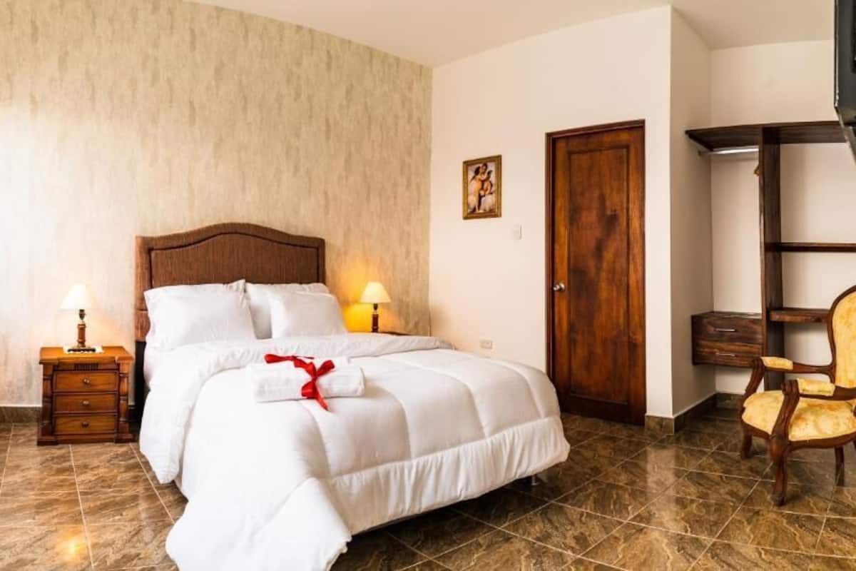 Une chambre d’hôtel avec un lit, des tables de chevet, une porte en bois, une chaise et une étagère.