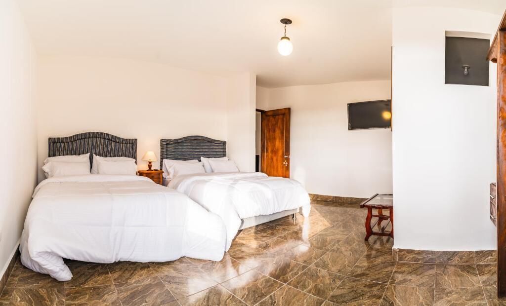 A hotel room with two beds, a wooden door, a small table, and a TV on the wall.
