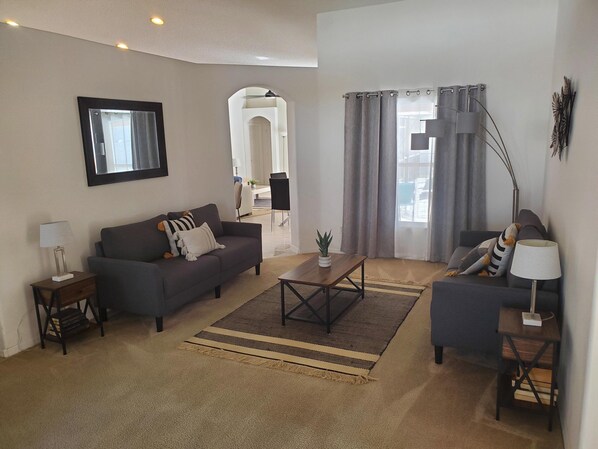 A living room with a sofa, a coffee table, a side table, and a lamp. There is a plant on the coffee table and a rug on the floor.