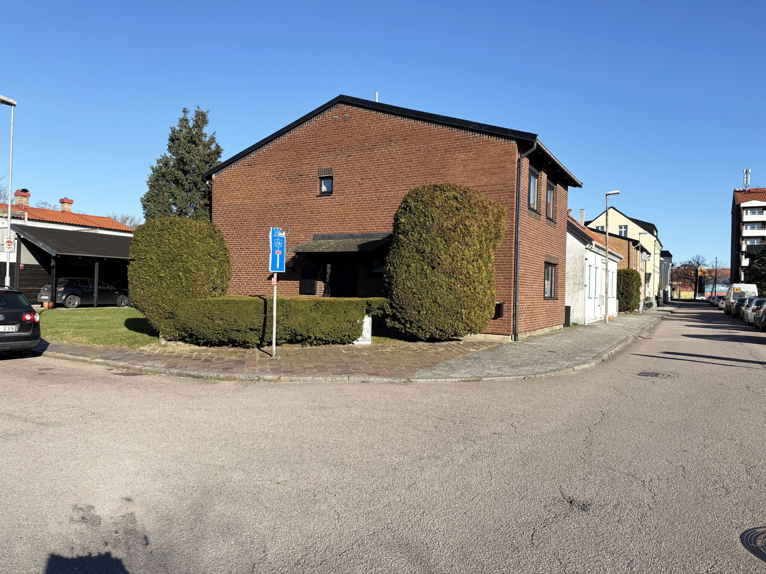 Un bâtiment en briques avec un garage, un panneau de signalisation de stationnement bleu et une haie bien entretenue.