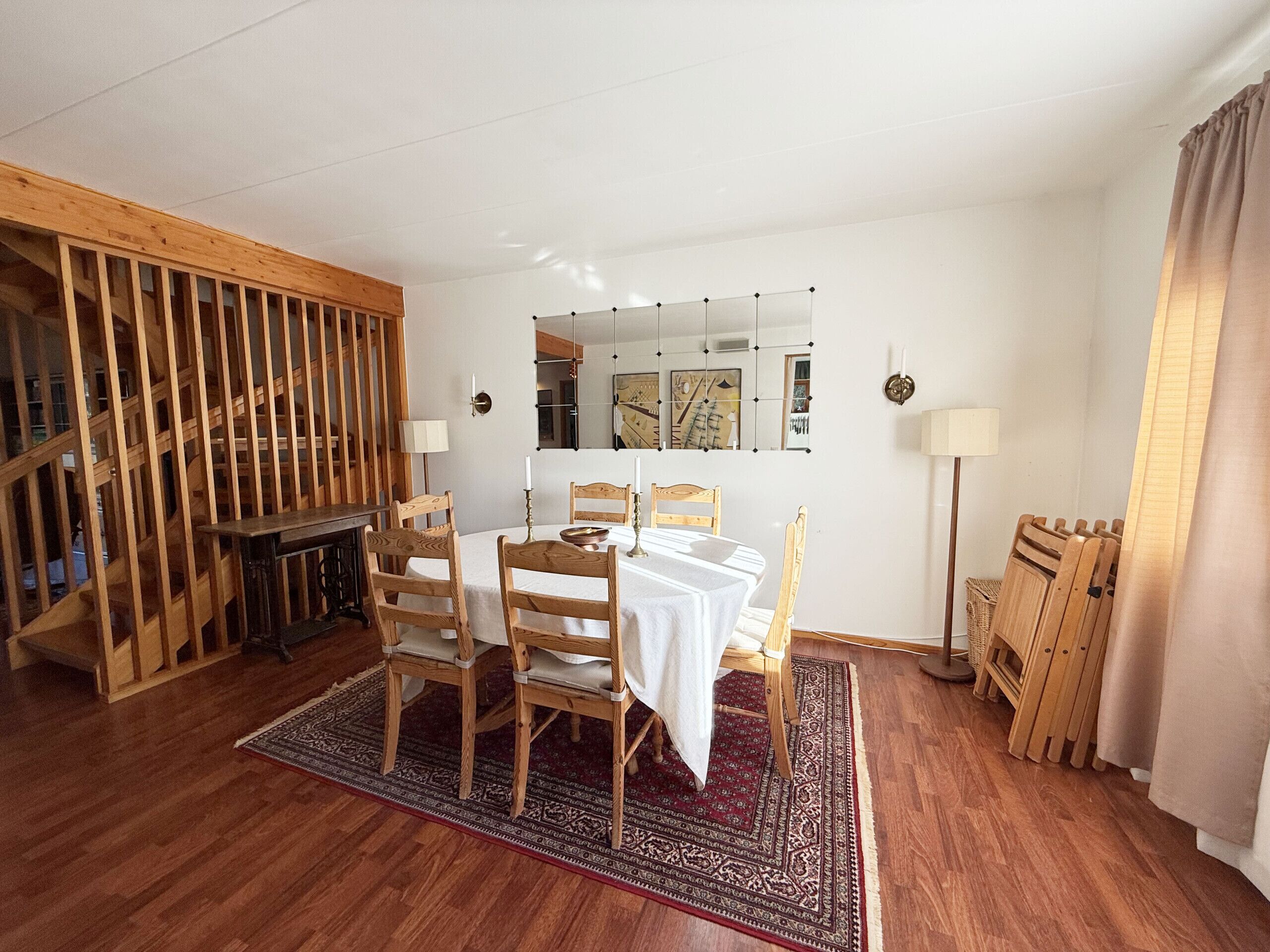 A room with a dining table, chairs, a patterned rug, wooden furniture, and a mirror on the wall.