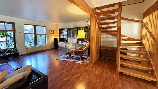 Ein geräumiges Zimmer mit Holzböden, einer Treppe, einem Bücherregal und einem Fenster mit Pflanzen.