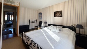 Ein Hotelzimmer mit einem großen Bett, einem Schreibtisch, einem Sessel, einem Kleiderschrank und einer Tür zu einem weiteren Raum.
