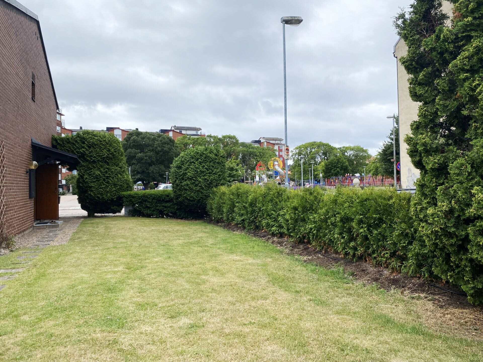 A grassy courtyard with a brick building, a street lamp, and a hedge.