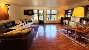 Ein geräumiges Wohnzimmer mit einer Couch, einem Couchtisch, einem Fernseher, einem Bücherregal und einem Fenster mit Blick.