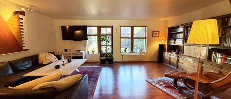 A spacious living room with a sofa, a coffee table, a TV, a bookshelf, and a window with a view.