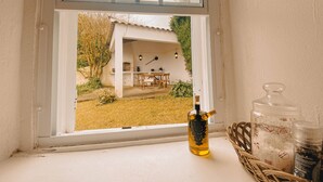 A window with a bottle of oil and jars on the windowsill, overlooking a patio area with a table and chairs. - Sun Island Retreat - Great Sunny Island/Sea view (Vila do Porto)
