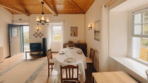 A dining area with a round table set for four, wooden chairs, a chandelier, and a window with a view of the outdoors. - Sun Island Retreat - Great Sunny Island/Sea view (Vila do Porto)